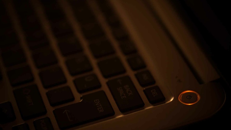 Close-up of a laptop keyboard in dim, warm lighting, with an orange-glowing power button creating a sleek, moody atmosphere.